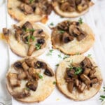 Mushroom gruyere tartlets garnished with thyme on white serving platter.