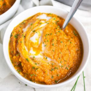 Roasted carrot soup in small white bowl with spoon.