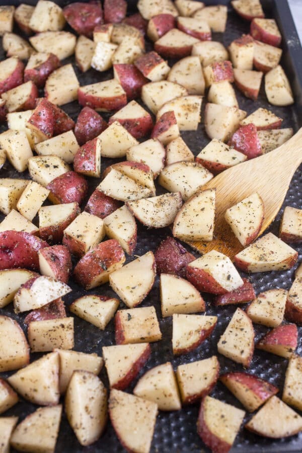 Uncooked diced red potatoes tossed in olive oil and spices on baking sheet.