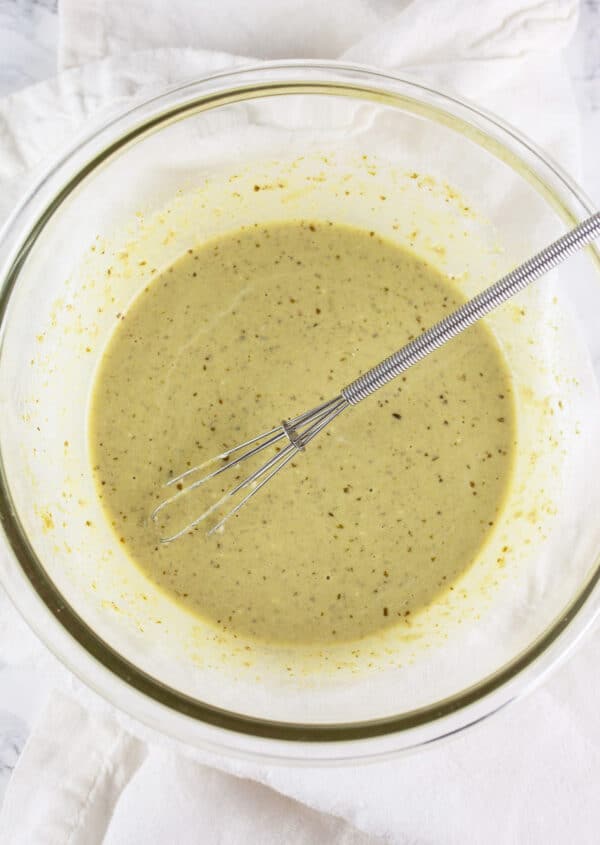 Creamy pesto mayo sauce in small glass bowl with whisk.