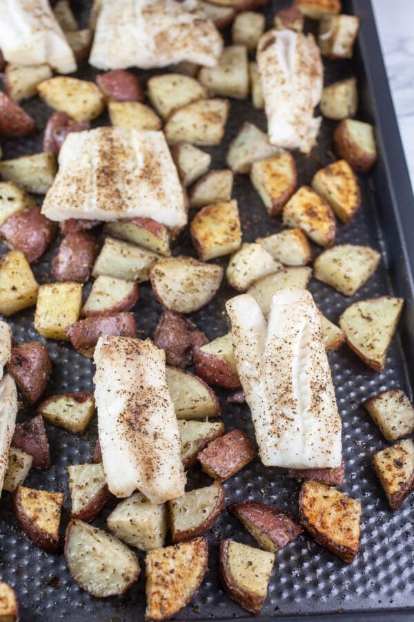 Baked cod filets and diced potatoes on baking sheet.