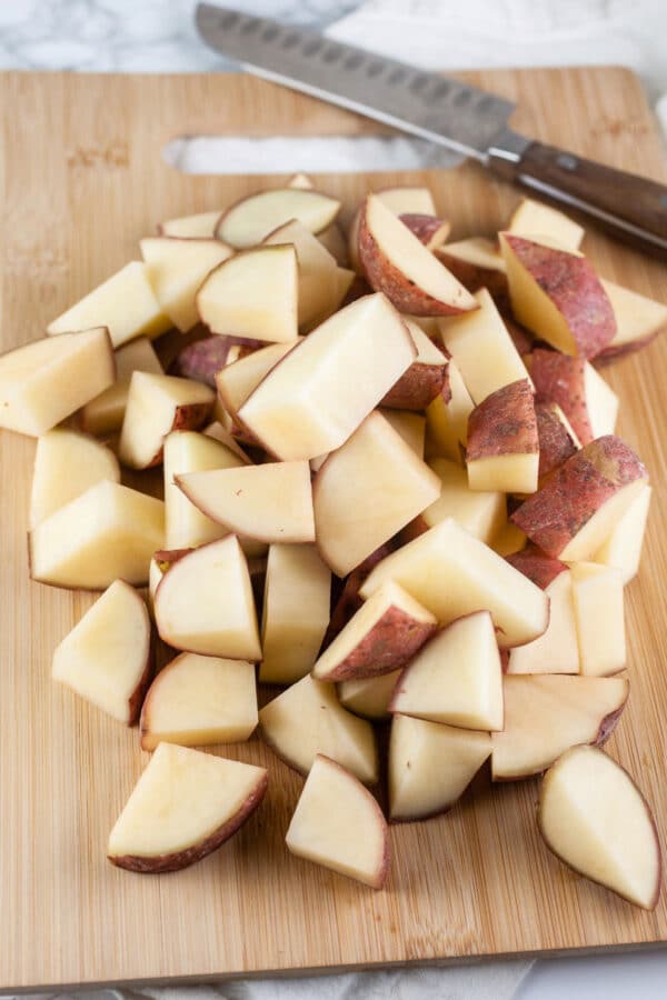 Diced red potatoes on wooden cutting board with knife.