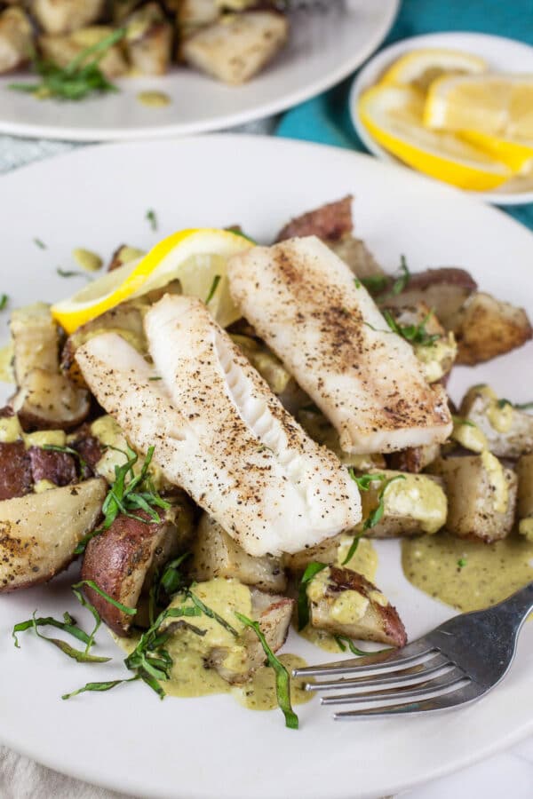 Roasted cod with potatoes and pesto mayo on white plate with fork.