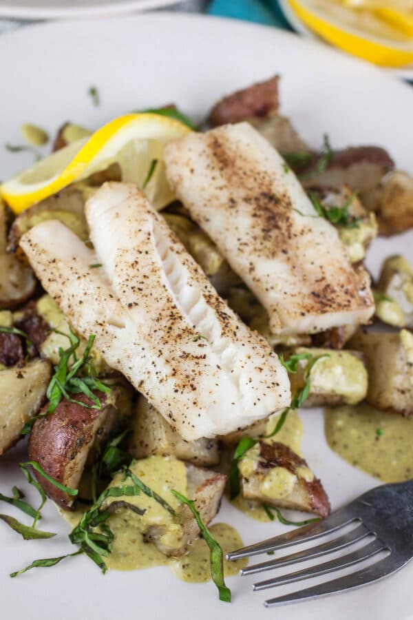 Sheet pan pesto cod with potatoes, sauce, and lemon on white plate.