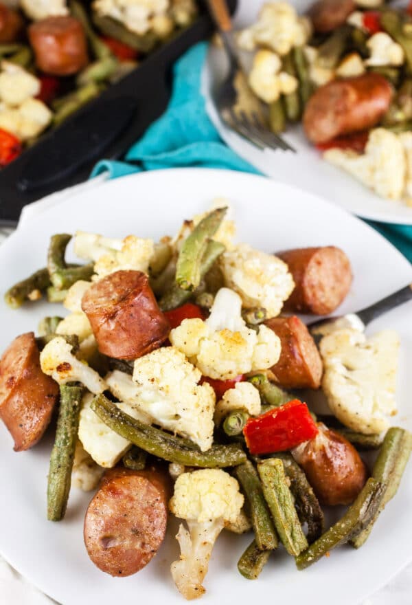 Sheet pan sausages with cauliflower, green beans, and red bell peppers on white plate.