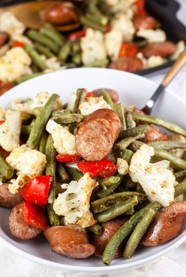 One pan chicken sausage with cauliflower, green beans, and red bell peppers in white bowl.