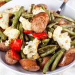 Sheet pan chicken sausage with green beans, cauliflower, and red bell peppers in white bowl.