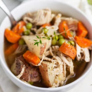 Slow cooker chicken potato soup in small white bowl with spoon.