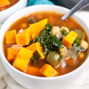 Sweet potato kale soup in small white bowl with spoon.