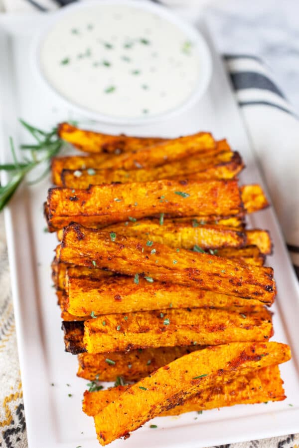 Air fryer butternut squash fries with rosemary dipping sauce on white platter.