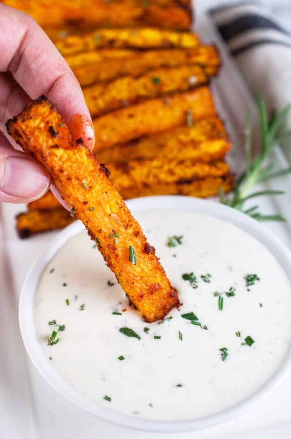 Butternut squash fries dipped into rosemary dipping sauce on white platter.