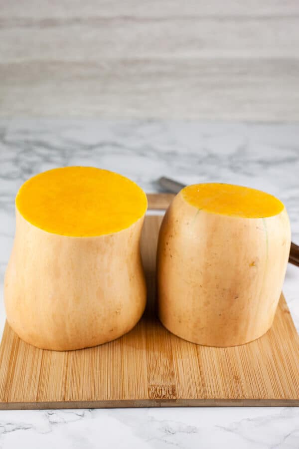 Butternut squash cut into halves standing on wooden cutting board.