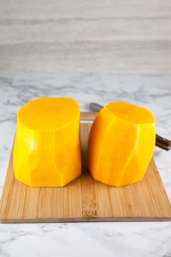 Peeled butternut squash cut into halves standing on wooden cutting board.