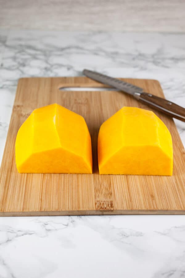 Half of peeled butternut squash cut into halves on wooden cutting board.