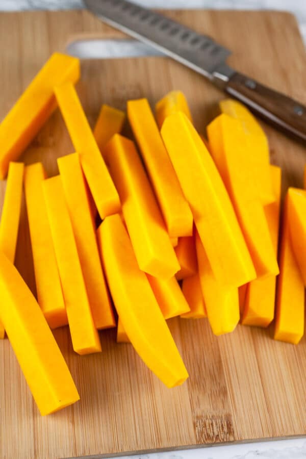 Butternut squash cut into fries on wooden cutting board.