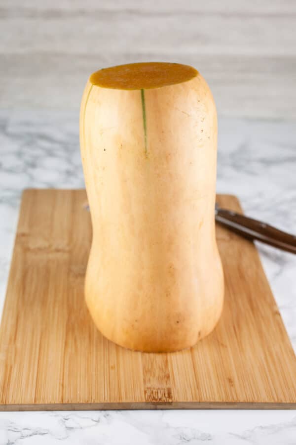 Top and bottom cut off standing butternut squash on wooden cutting board.