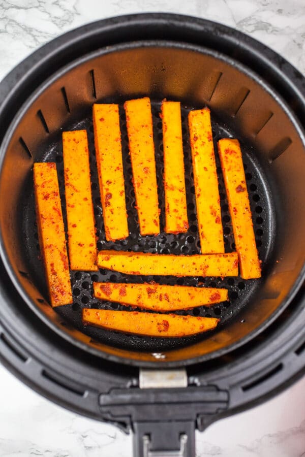 Uncooked squash fries in air fryer basket.
