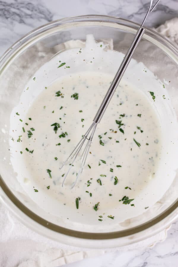 Rosemary garlic lemon dipping sauce in small glass bowl with whisk.