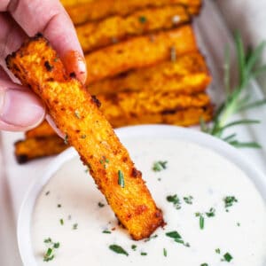 Butternut squash fries dipped into small bowl of rosemary dipping sauce.