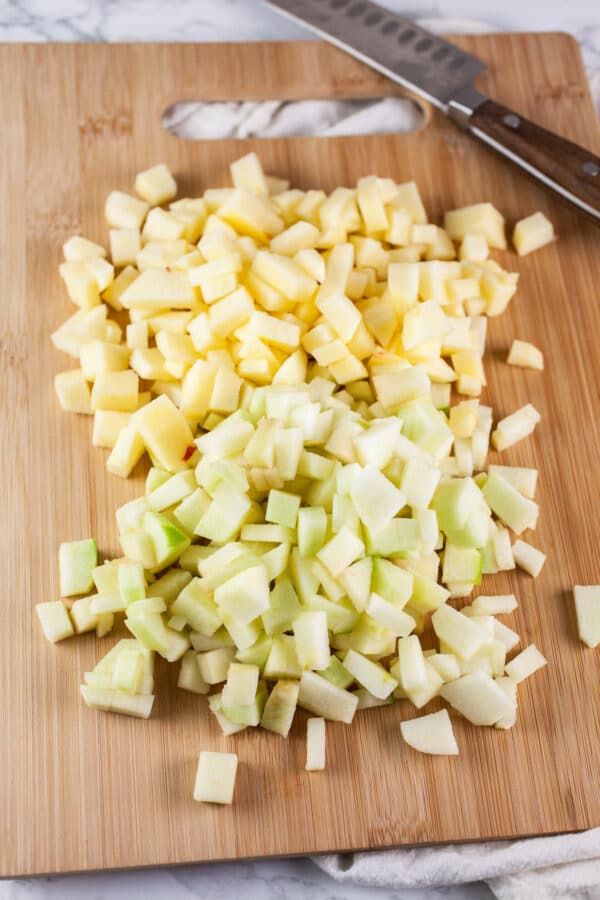 Diced, peeled Granny Smith and Gala apples on cutting board with knife.