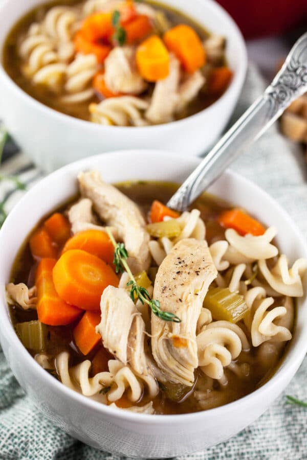 Dutch oven gluten free chicken noodle soup in small white bowls with spoons.