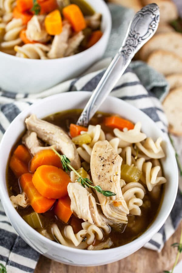 Gluten free chicken noodle soup with bread in small white bowls and spoons.