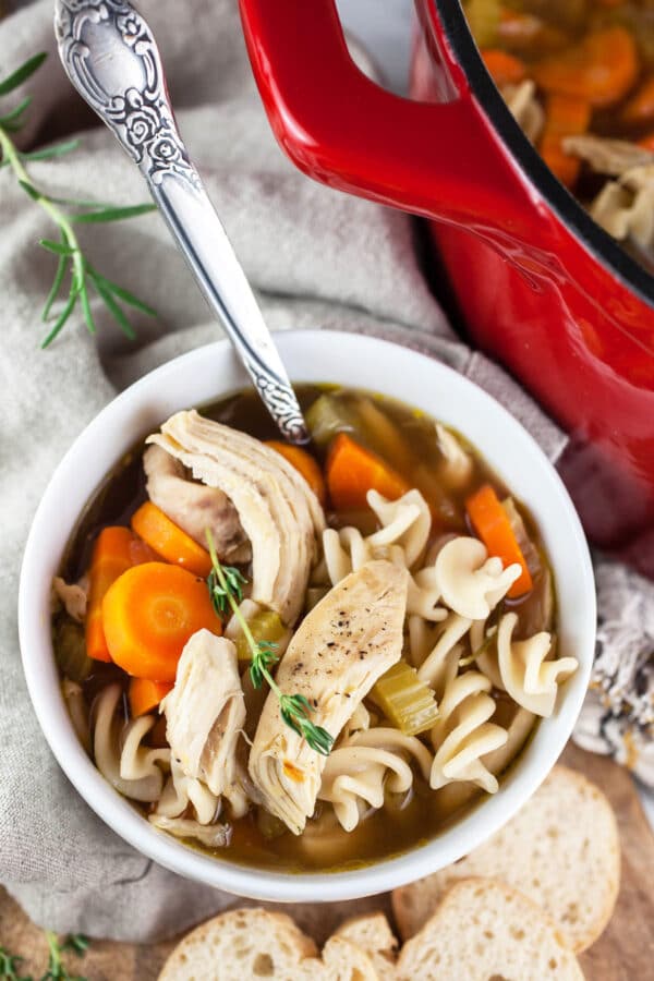 Homemade chicken noodle soup in small white bowl with pieces of bread.