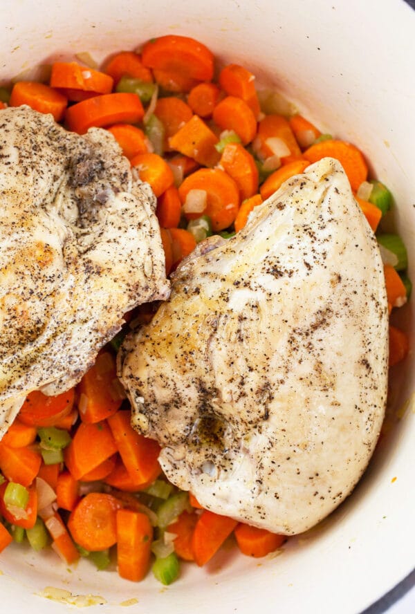 Seared bone-in chicken breasts on top of sautéed vegetables in white Dutch oven. 