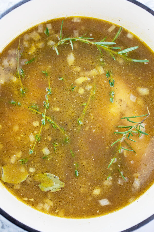 Chicken broth, chicken breasts, and fresh thyme and rosemary in white Dutch oven.