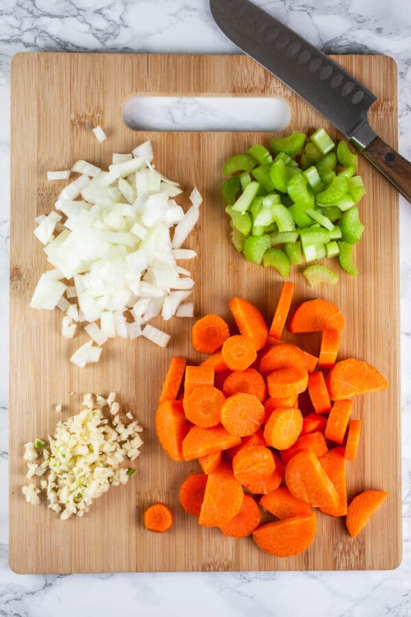 Minced garlic, onions, celery, and carrots on wooden cutting board.