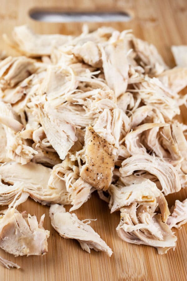 Shredded cooked chicken breasts on wooden cutting board.