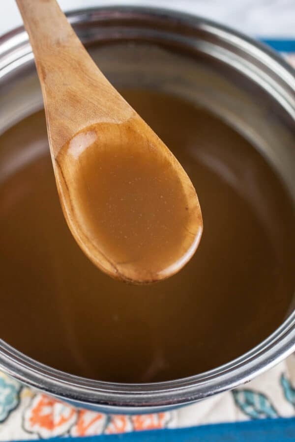 Spoonful of maple glaze lifted from small sauce pan.