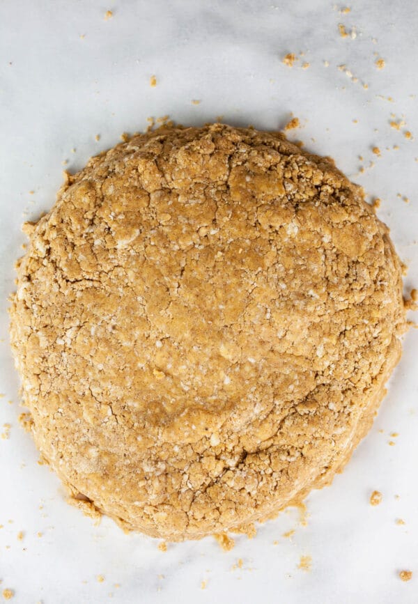 Round disc of pumpkin scone dough on white surface.