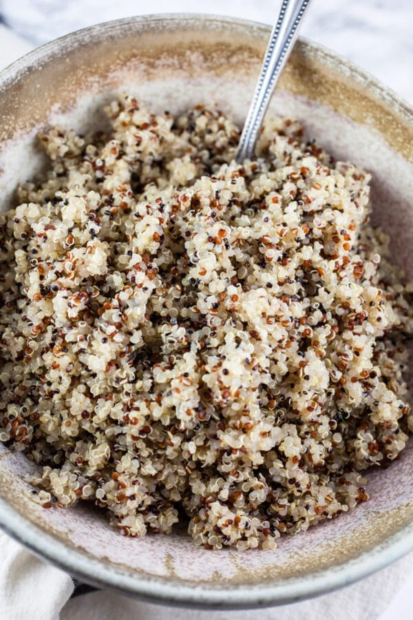 Looking for new ways to enjoy squash? Try this Roasted Butternut Squash, Kale, and Farro Salad. This healthy butternut squash salad is tossed with kale and farro for a sweet and savory fall side dish! It would make a great addition to a Thanksgiving or holiday dinner menu. #squash #butternutsquash #kale #farro #thanksgiving Cooked quinoa in ceramic bowl with spoon.
