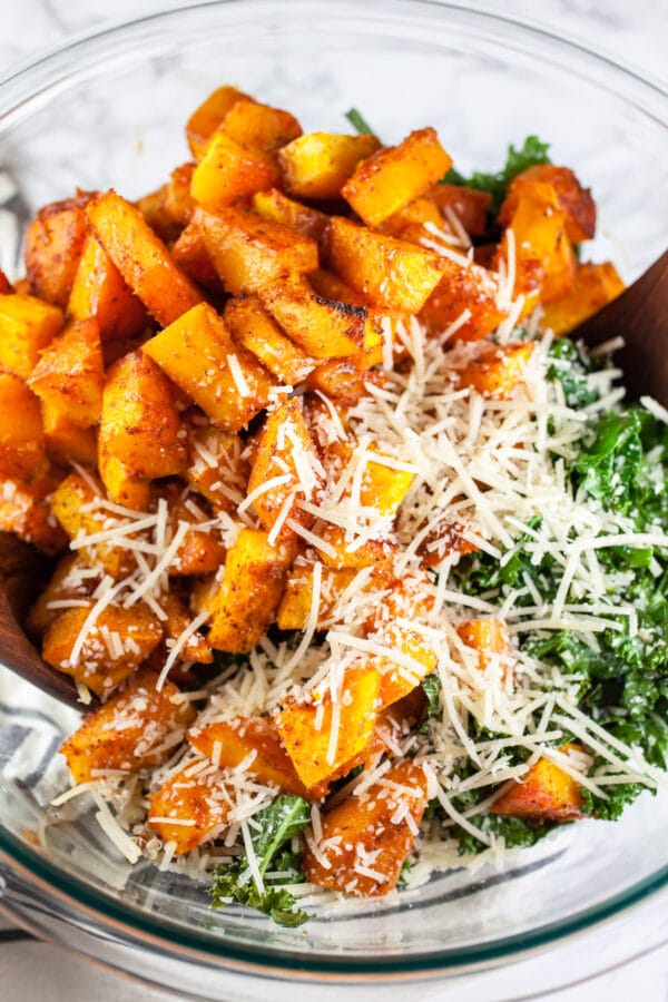 Roasted butternut squash, kale, and Parmesan cheese in large glass bowl.