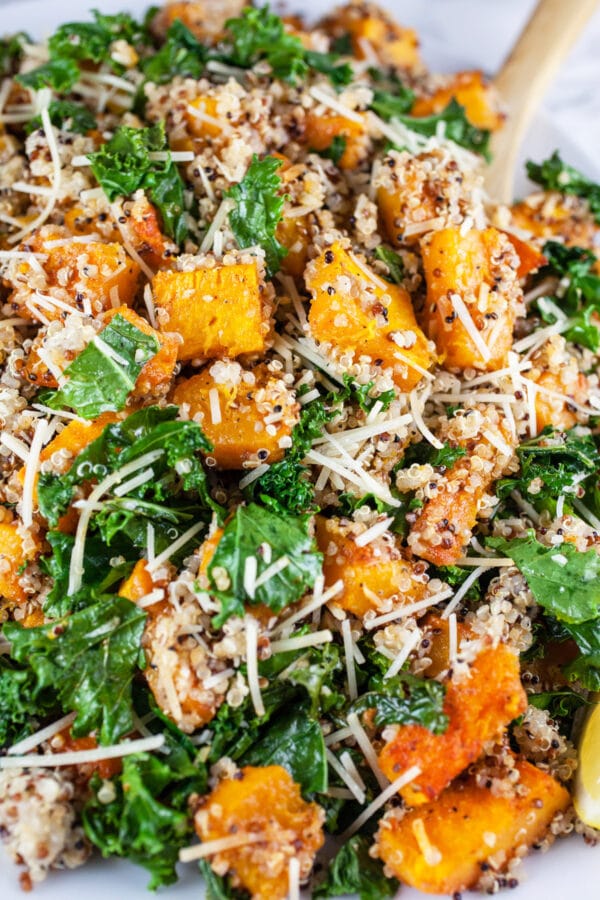 Looking for new ways to enjoy squash? Try this Roasted Butternut Squash, Kale, and Farro Salad. This healthy butternut squash salad is tossed with kale and farro for a sweet and savory fall side dish! It would make a great addition to a Thanksgiving or holiday dinner menu. #squash #butternutsquash #kale #farro #thanksgiving Butternut squash, kale, and quinoa salad with Parmesan cheese on serving platter.