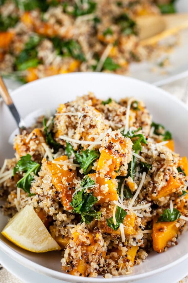 Roasted butternut squash quinoa kale salad in white bowl with fork.