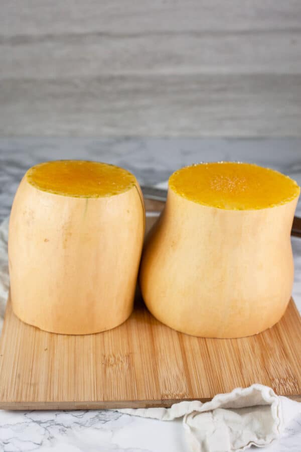 Butternut squash cut into halves standing on wooden cutting board.