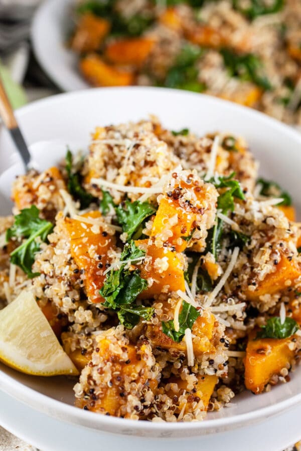 Looking for new ways to enjoy squash? Try this Roasted Butternut Squash, Kale, and Farro Salad. This healthy butternut squash salad is tossed with kale and farro for a sweet and savory fall side dish! It would make a great addition to a Thanksgiving or holiday dinner menu. #squash #butternutsquash #kale #farro #thanksgiving Roasted butternut squash quinoa kale salad in white bowls.