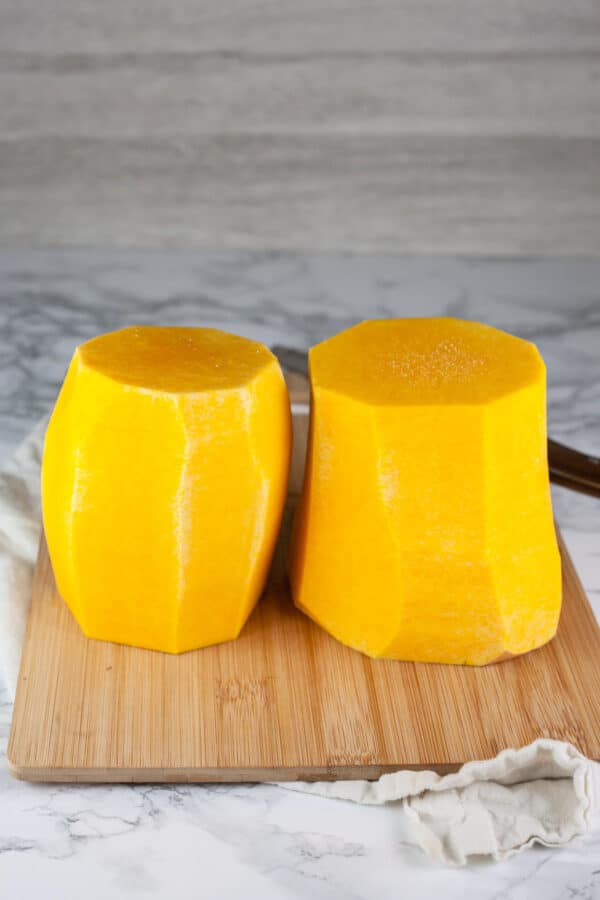 Peeled butternut squash cut into halves standing on wooden cutting board.
