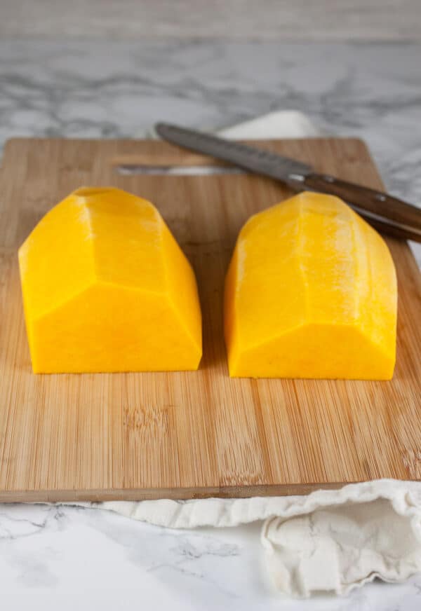 Half of peeled butternut squash cut into halves on wooden cutting board.