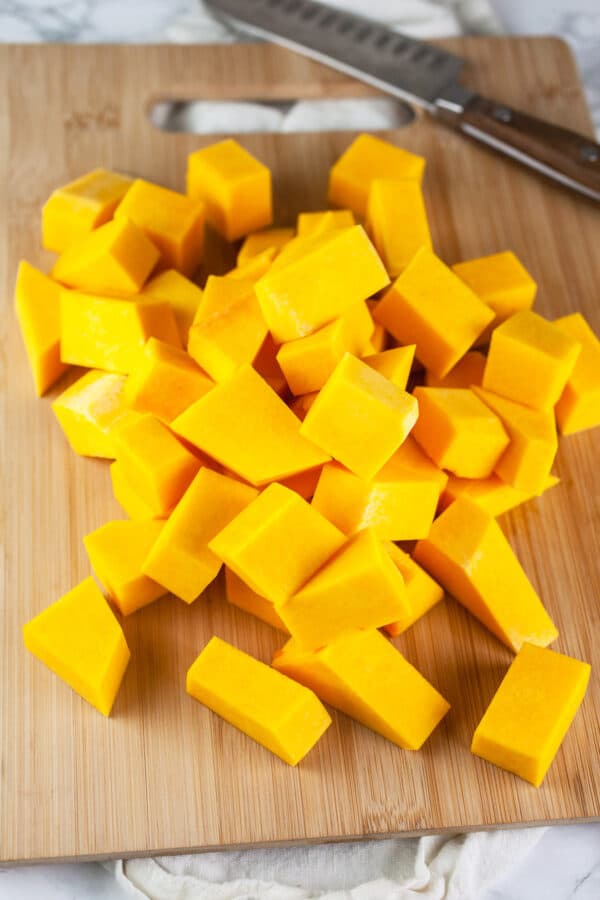 Butternut squash chunks on wooden cutting board with knife.