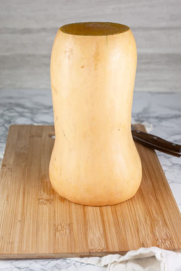 Top and bottom cut off butternut squash standing on wooden cutting board.