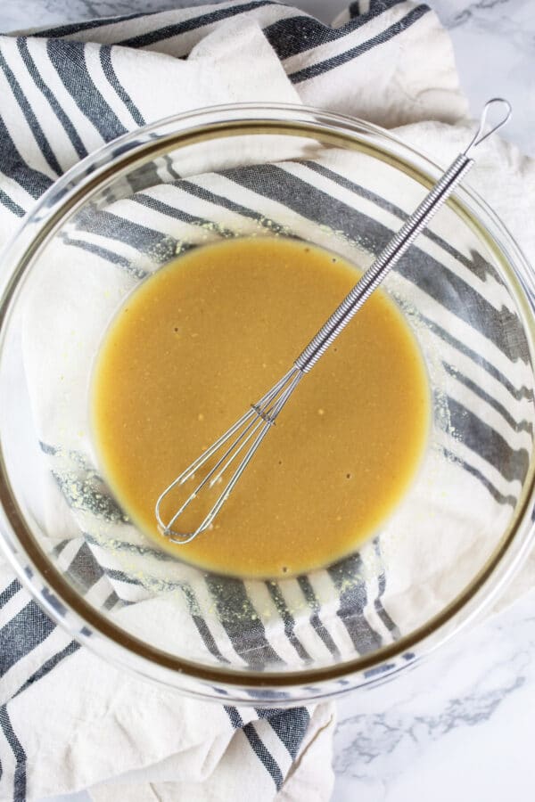 Maple syrup Dijon mustard glaze in small glass bowl with whisk.