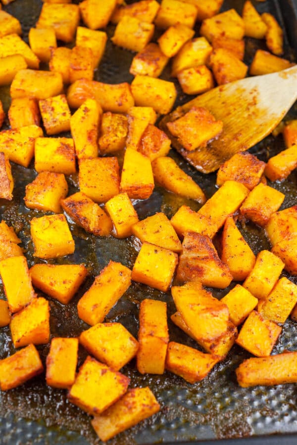 Looking for new ways to enjoy squash? Try this Roasted Butternut Squash, Kale, and Farro Salad. This healthy butternut squash salad is tossed with kale and farro for a sweet and savory fall side dish! It would make a great addition to a Thanksgiving or holiday dinner menu. #squash #butternutsquash #kale #farro #thanksgiving Roasted butternut squash tossed in maple Dijon glaze on baking sheet.