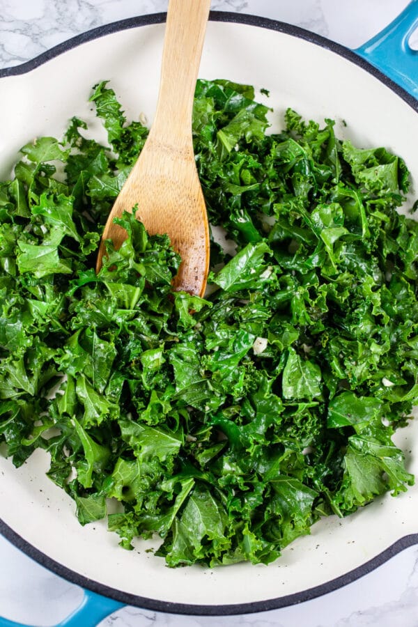 Looking for new ways to enjoy squash? Try this Roasted Butternut Squash, Kale, and Farro Salad. This healthy butternut squash salad is tossed with kale and farro for a sweet and savory fall side dish! It would make a great addition to a Thanksgiving or holiday dinner menu. #squash #butternutsquash #kale #farro #thanksgiving Kale sautéed with garlic in white cast iron skillet.