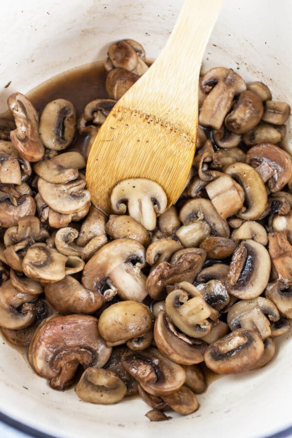 Sliced mushrooms sautéed in white Dutch oven.