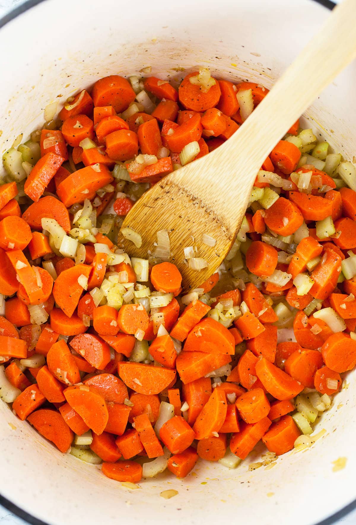 Sliced carrots sautéed with garlic, onions, and celery in white Dutch oven.