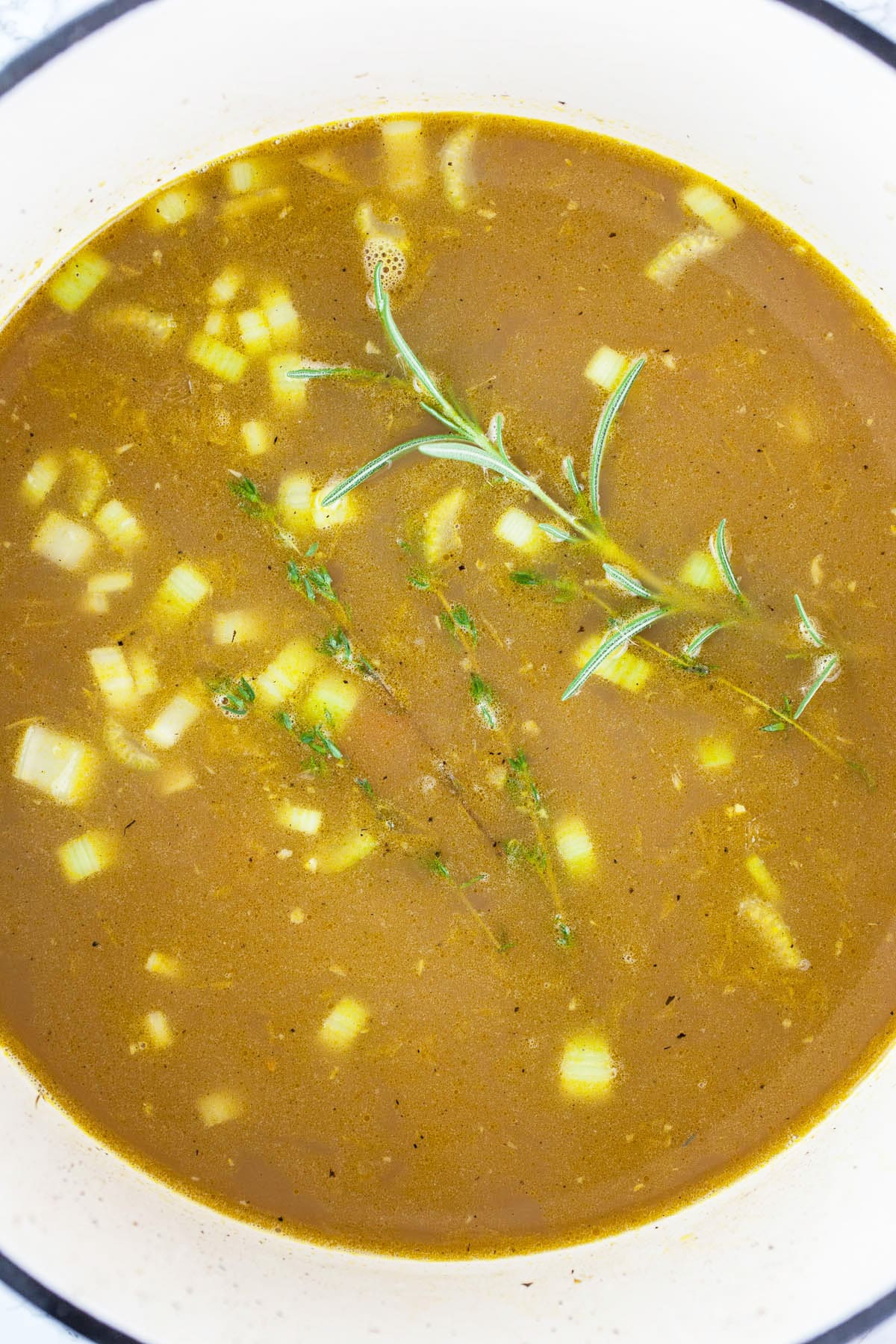 Chicken broth, thyme, and rosemary sprigs in white Dutch oven.