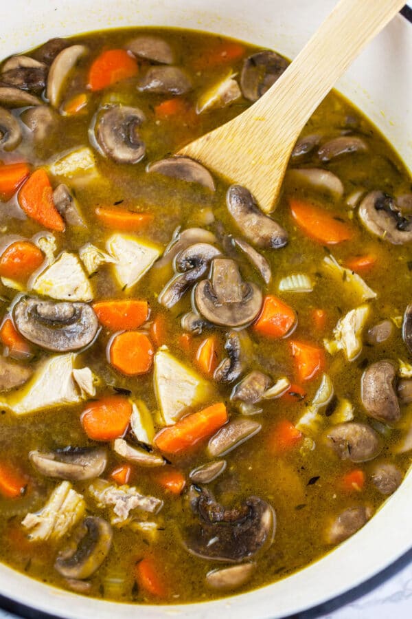 Wild rice soup with chunks of turkey and mushrooms in white Dutch oven.